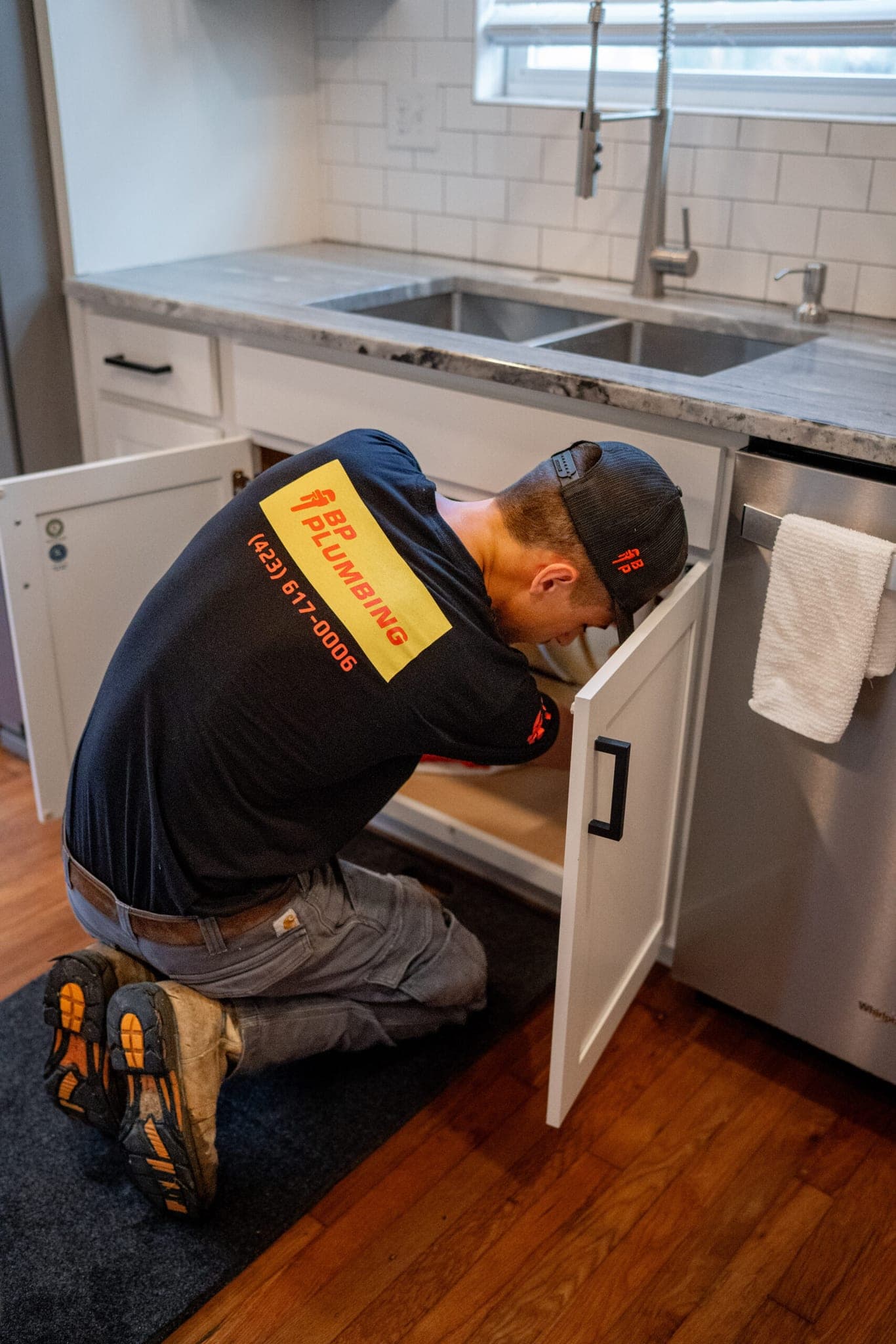 A BP Plumbing technician working in the cabinet under a kitchen sink